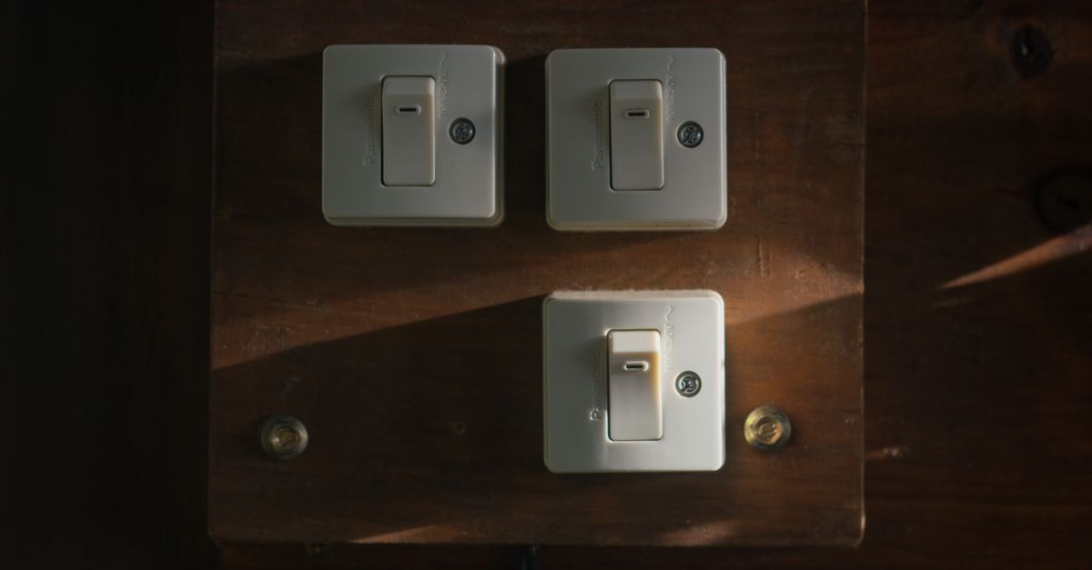 Close-up view of vintage light switches mounted on a wooden panel, illuminated softly in a dark interior setting.